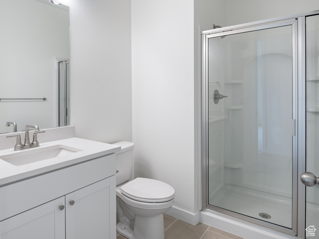 Bathroom featuring toilet, vanity with extensive cabinet space, tile flooring, and a shower with shower door