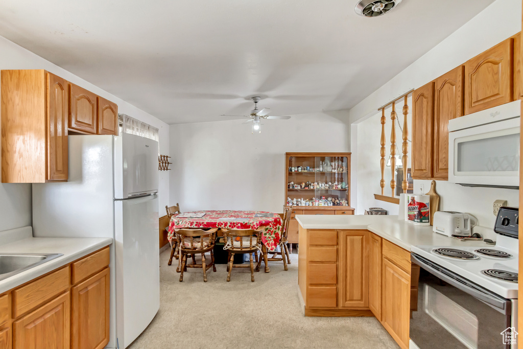 Kitchen with white appliances, light colored carpet, sink, and ceiling fan