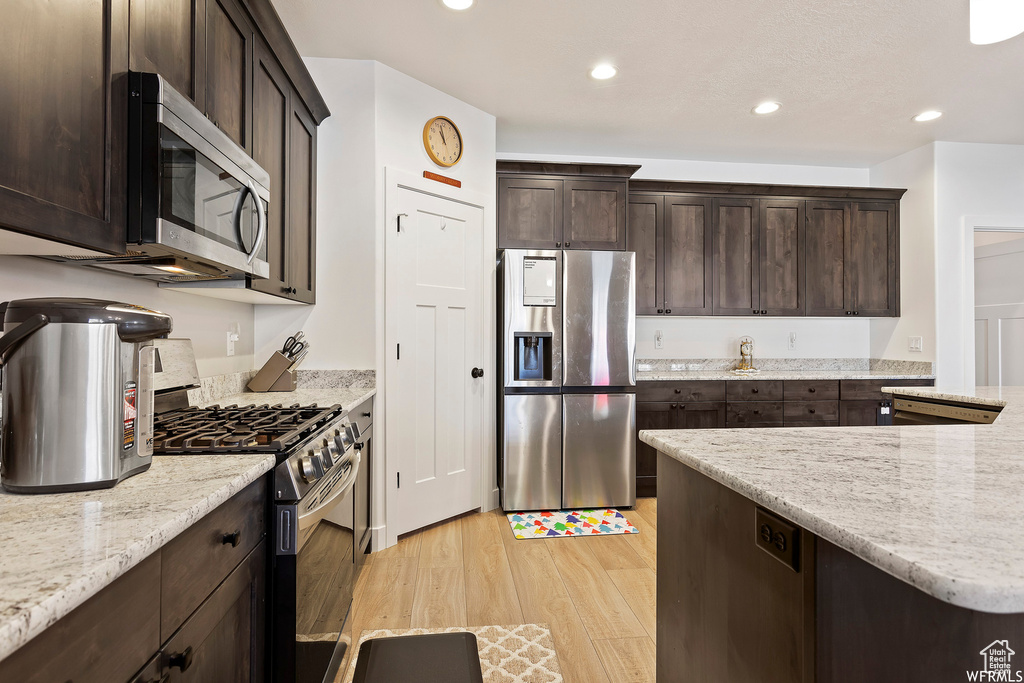 Kitchen with stainless steel appliances, light wood-type flooring, light stone countertops, and dark brown cabinetry