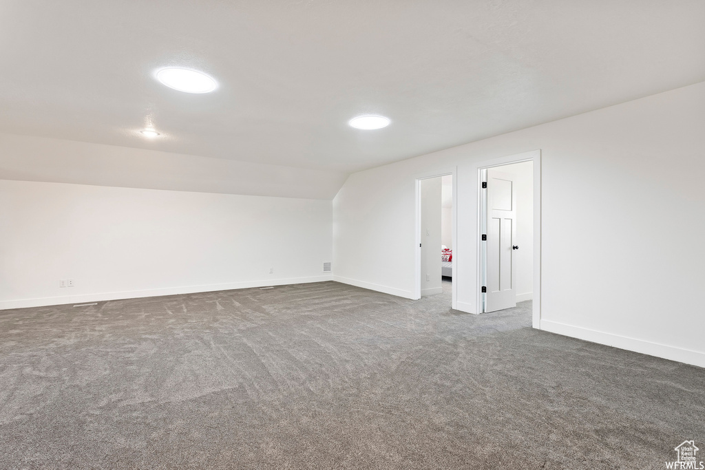 Empty room featuring dark colored carpet and lofted ceiling