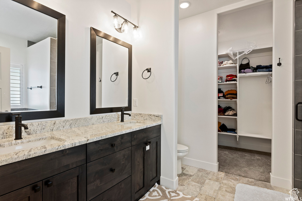 Bathroom with tile flooring, vanity with extensive cabinet space, dual sinks, and toilet