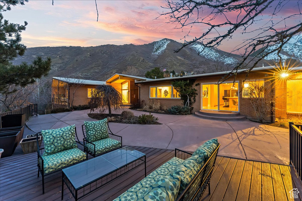 Back house at dusk featuring a deck with mountain view, outdoor lounge area, and a patio