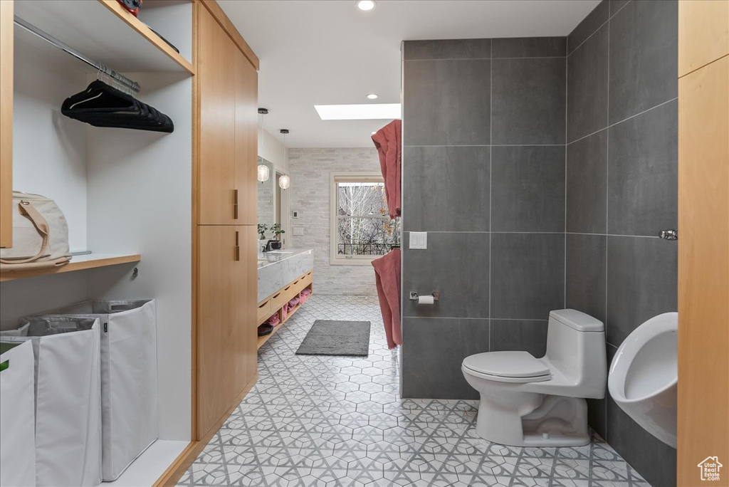 Bathroom featuring vanity, a skylight, tile walls, toilet, and tile flooring
