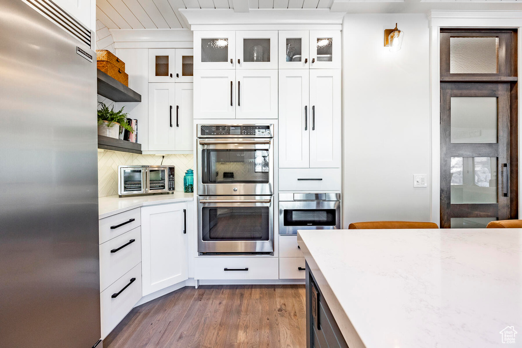 Kitchen with backsplash, wall chimney exhaust hood, dark hardwood / wood-style floors, stainless steel appliances, and white cabinets