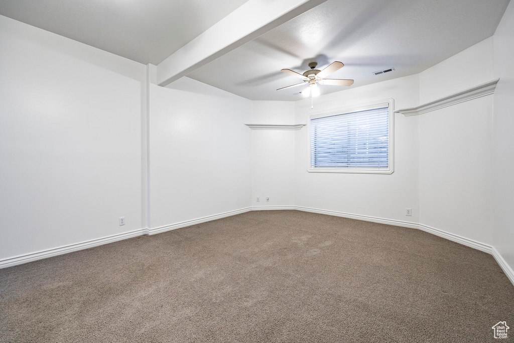 Empty room with ceiling fan, beam ceiling, and carpet flooring