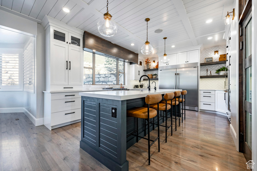 Kitchen featuring backsplash, white cabinetry, built in fridge, an island with sink, and wood-type flooring