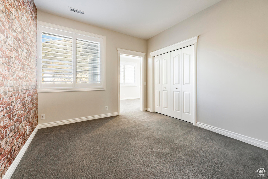 Unfurnished bedroom featuring a closet, brick wall, and carpet flooring