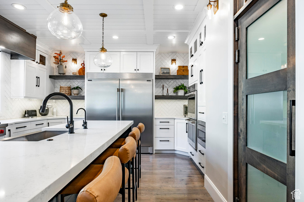 Kitchen with backsplash, stainless steel built in fridge, white cabinets, dark wood-type flooring, and hanging light fixtures