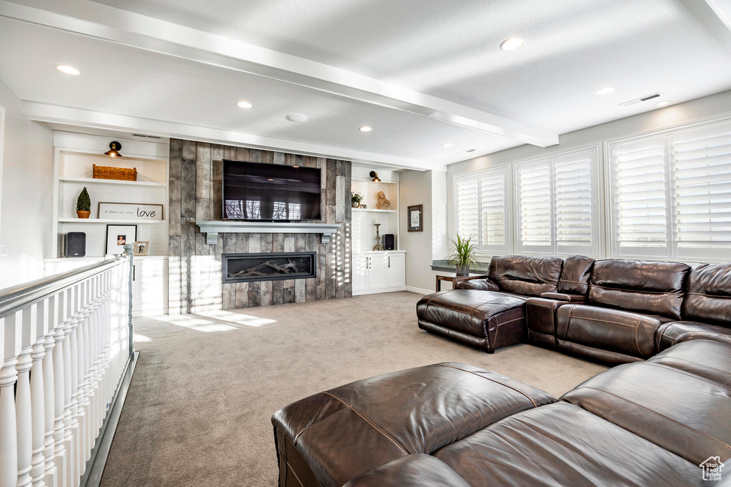 Living room with a fireplace, built in features, beamed ceiling, and light colored carpet