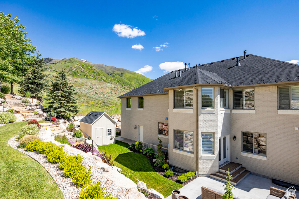 View of property exterior featuring a patio, a shed, a mountain view, and a lawn