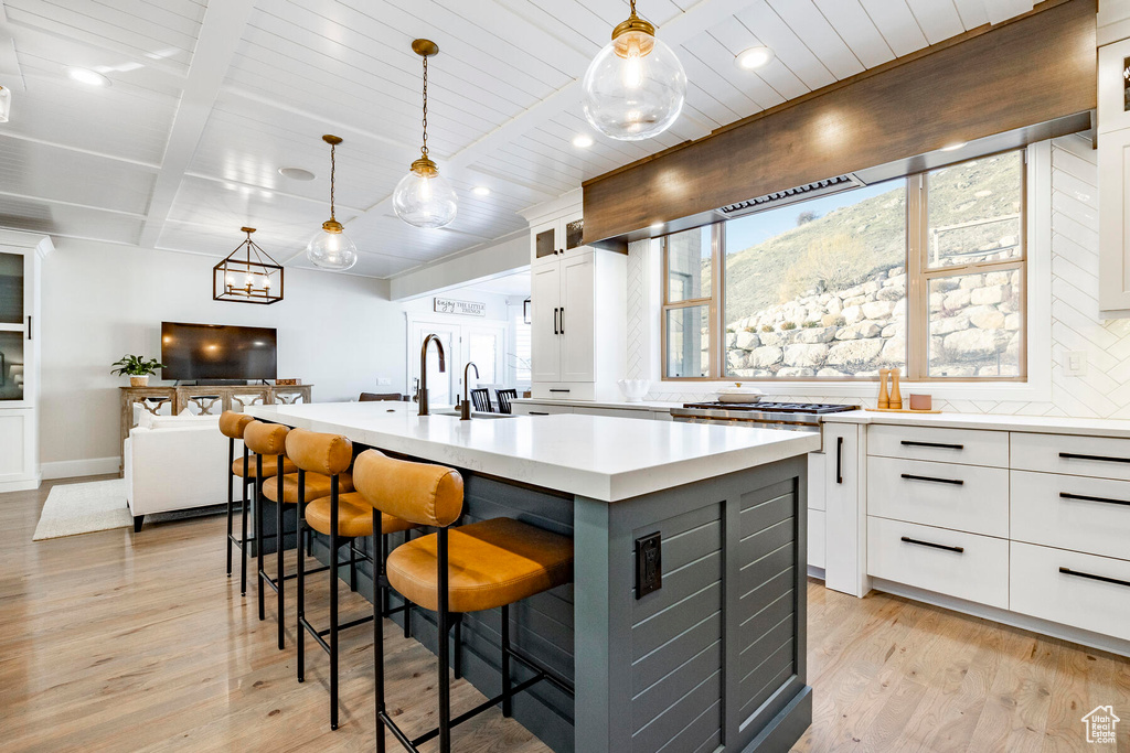 Kitchen with a kitchen island with sink, hanging light fixtures, light hardwood / wood-style flooring, and white cabinetry