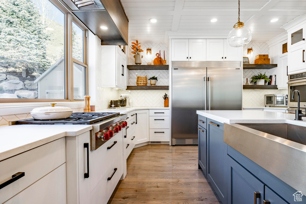 Kitchen with appliances with stainless steel finishes, backsplash, blue cabinetry, light wood-type flooring, and pendant lighting