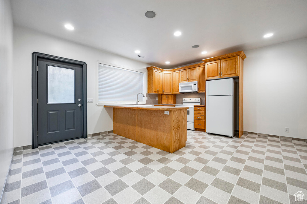 Kitchen featuring sink, kitchen peninsula, white appliances, and light tile patterned floors