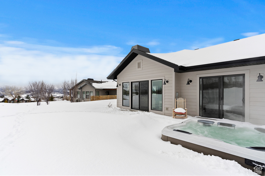 Snow covered back of property featuring an outdoor hot tub