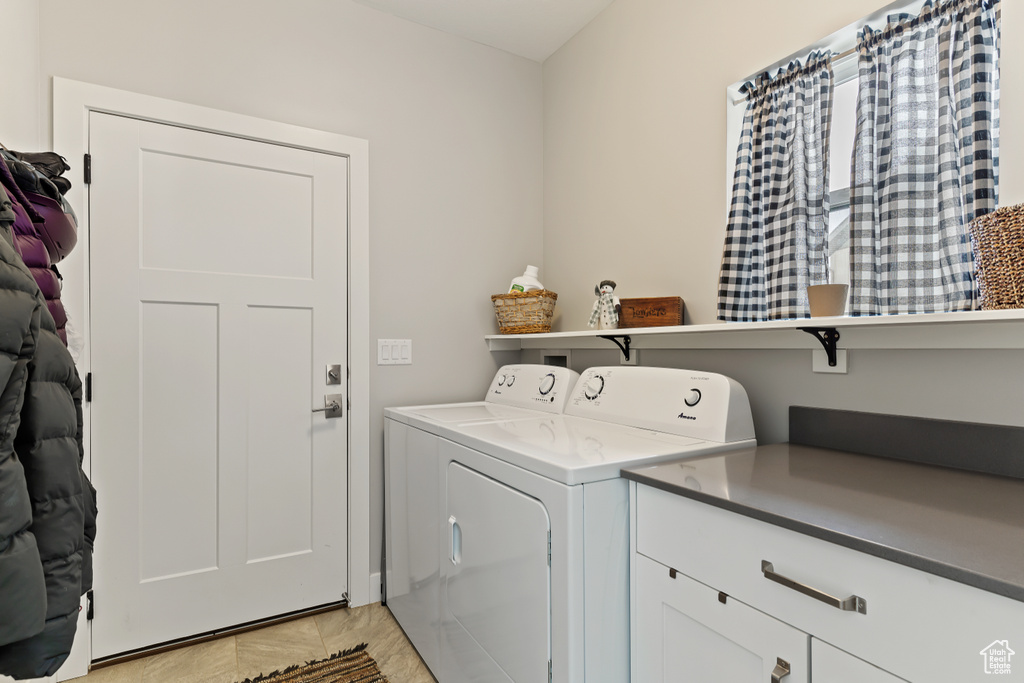 Clothes washing area with cabinets, washing machine and dryer, and light tile floors