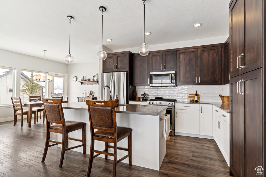 Kitchen with a notable chandelier, decorative light fixtures, dark hardwood / wood-style flooring, a center island with sink, and appliances with stainless steel finishes