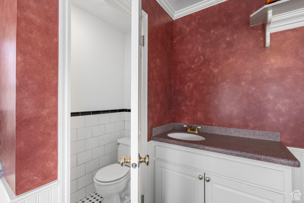Bathroom featuring tile floors, tile walls, toilet, ornamental molding, and vanity