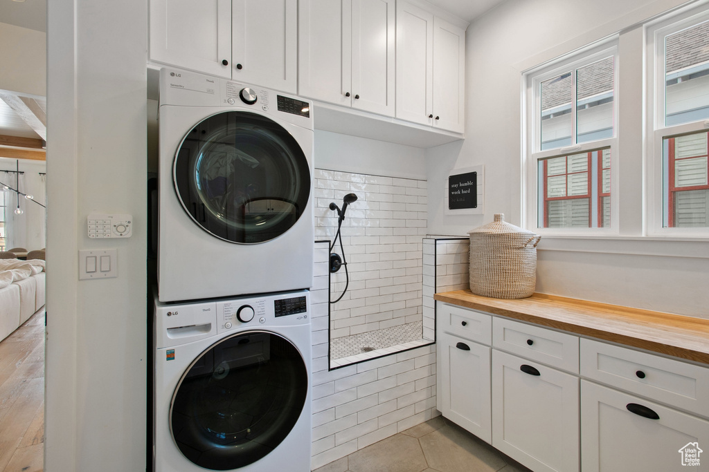 Washroom featuring stacked washer / drying machine, hookup for an electric dryer, cabinets, and light tile floors