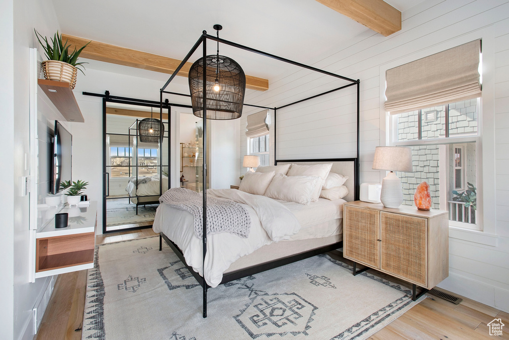 Bedroom featuring an inviting chandelier, light hardwood / wood-style flooring, a barn door, and beam ceiling