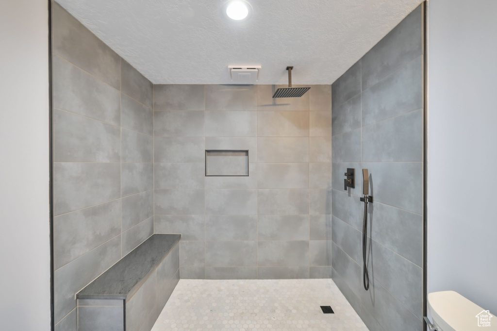 Bathroom featuring a textured ceiling, toilet, and tiled shower