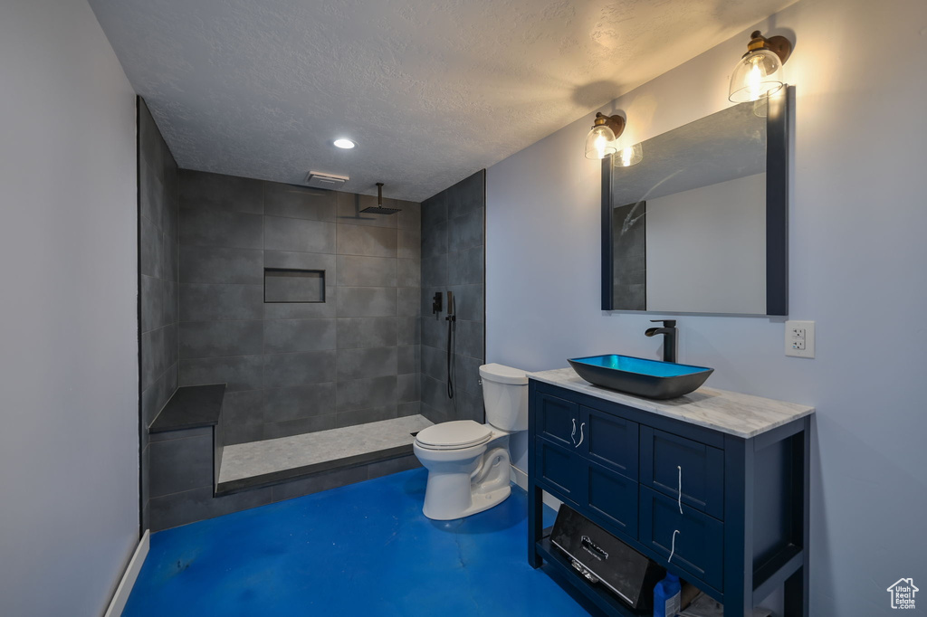 Bathroom with tiled shower, oversized vanity, a textured ceiling, and toilet