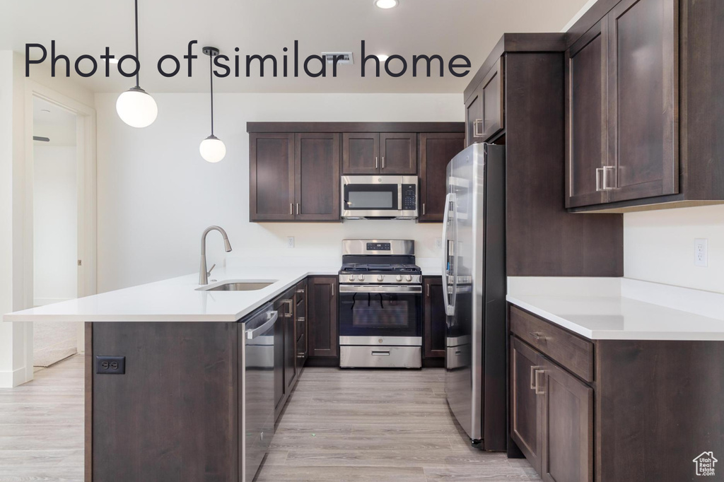 Kitchen with appliances with stainless steel finishes, light wood-type flooring, sink, and decorative light fixtures