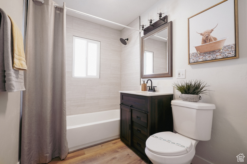 Full bathroom with wood-type flooring, toilet, shower / bathtub combination with curtain, and oversized vanity
