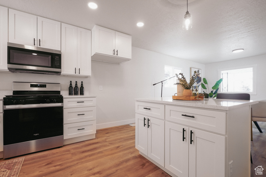 Kitchen with appliances with stainless steel finishes, pendant lighting, white cabinetry, and light hardwood / wood-style floors