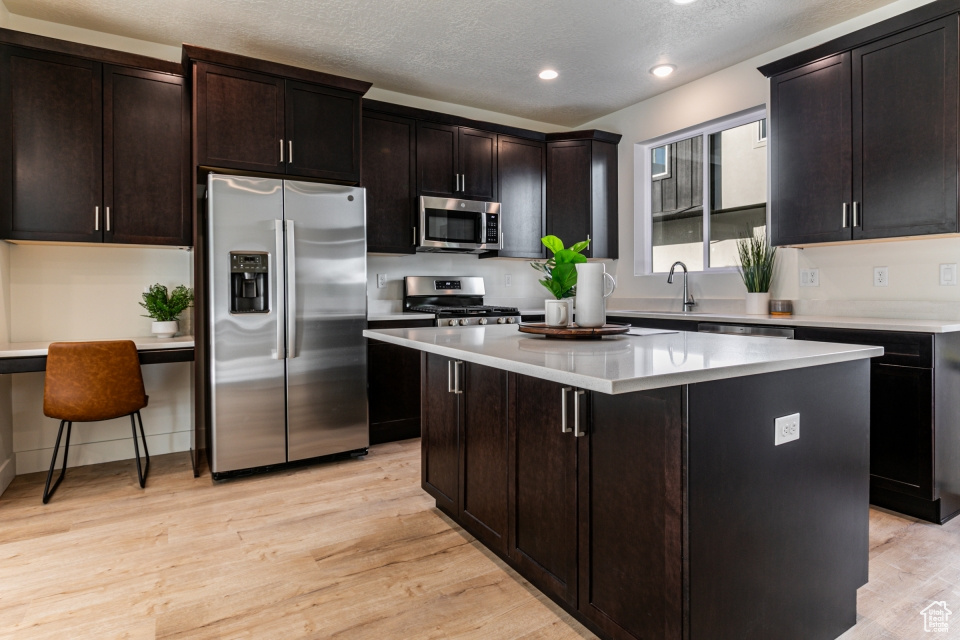 Kitchen with a kitchen island, light wood-type flooring, a kitchen breakfast bar, dark brown cabinets, and stainless steel appliances