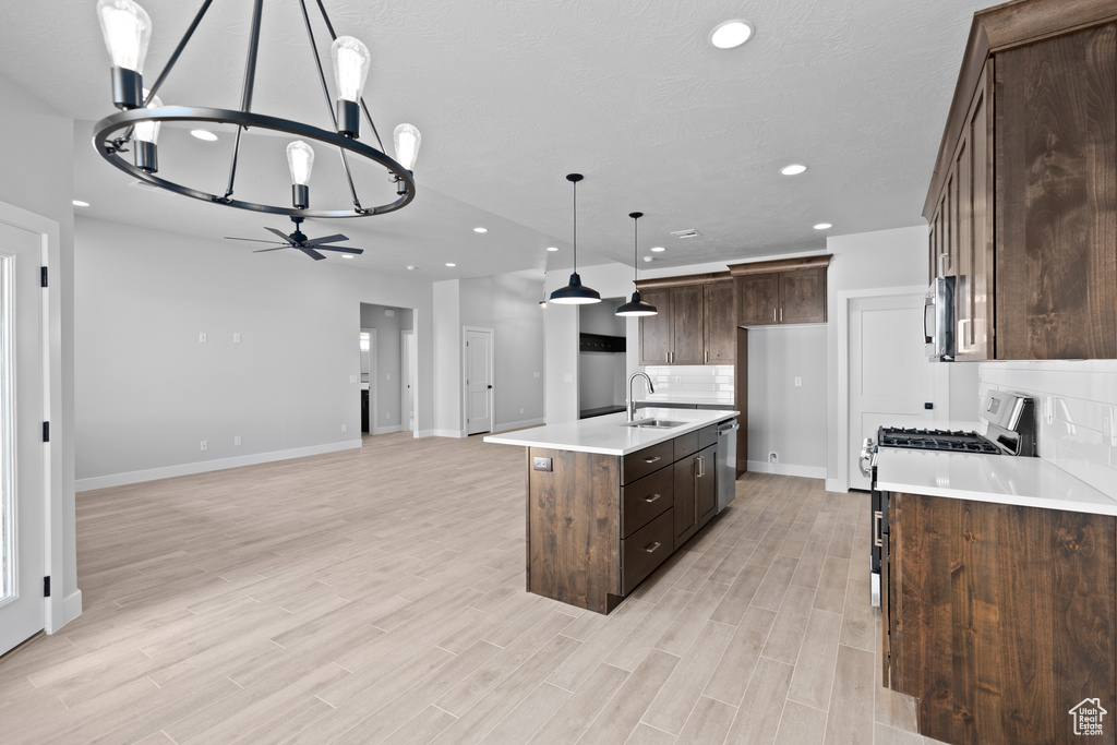 Kitchen featuring sink, pendant lighting, a center island with sink, light wood-type flooring, and dark brown cabinets