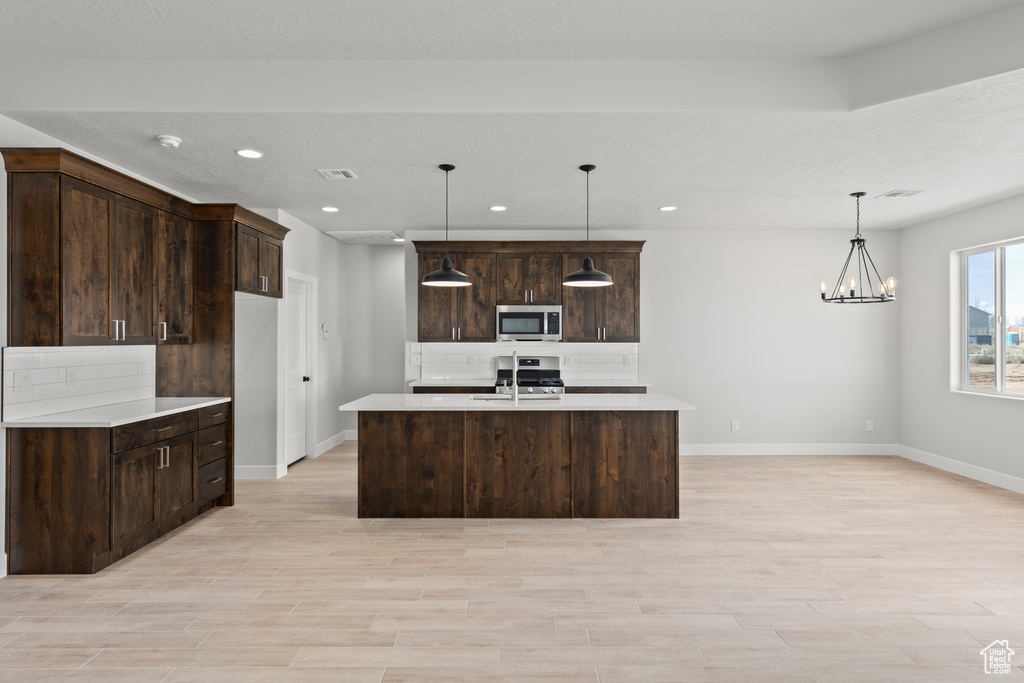 Kitchen featuring appliances with stainless steel finishes, a chandelier, tasteful backsplash, and dark brown cabinets