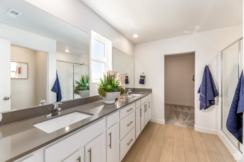 Bathroom featuring hardwood / wood-style flooring, dual sinks, a shower with door, and oversized vanity
