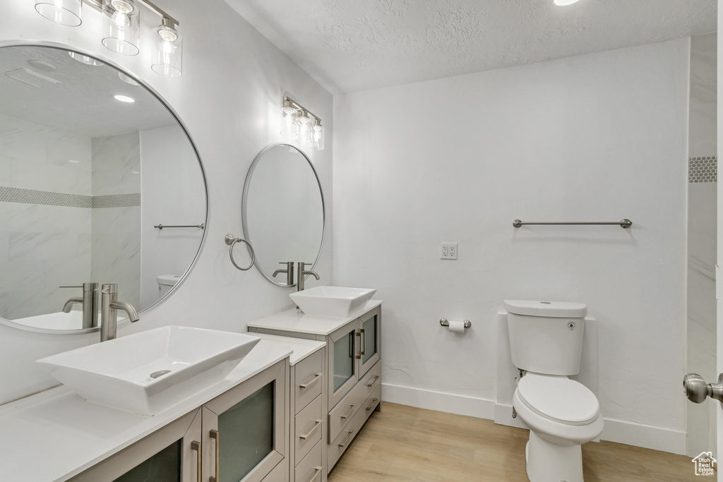 Bathroom featuring dual vanity, hardwood / wood-style flooring, a textured ceiling, and toilet