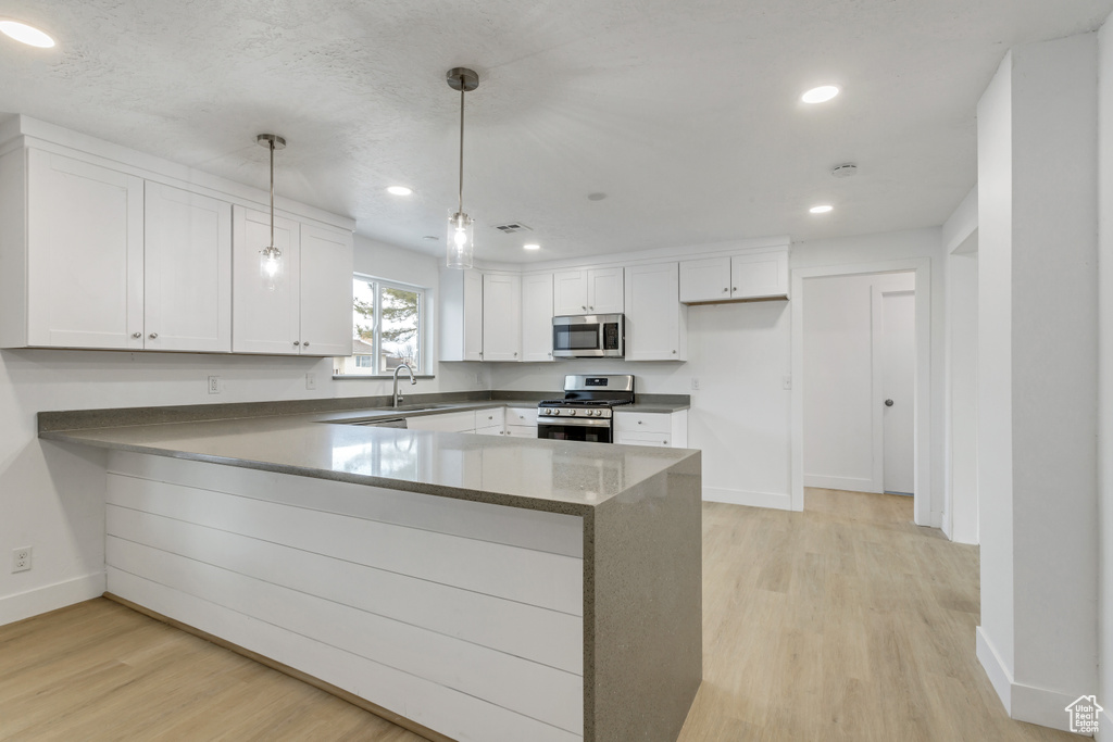 Kitchen with white cabinetry, light hardwood / wood-style floors, kitchen peninsula, hanging light fixtures, and stainless steel appliances
