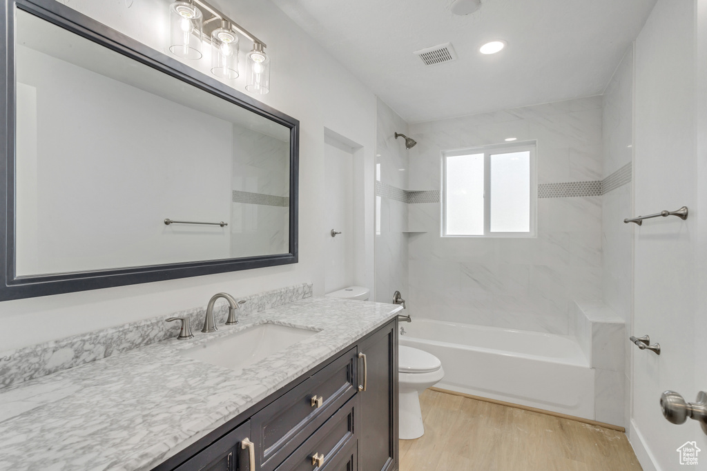 Full bathroom featuring toilet, tiled shower / bath combo, large vanity, and hardwood / wood-style floors