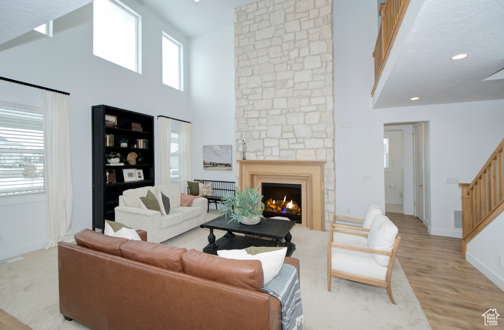 Living room with a stone fireplace, a high ceiling, and light hardwood / wood-style floors