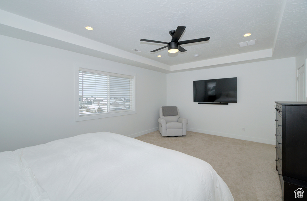 Bedroom featuring light colored carpet, a tray ceiling, and ceiling fan