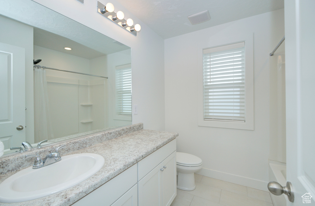 Full bathroom with a wealth of natural light, toilet, tile floors, oversized vanity, and shower / tub combo with curtain