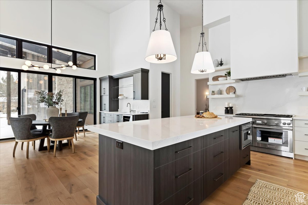 Kitchen with a towering ceiling, hanging light fixtures, light hardwood / wood-style flooring, range with two ovens, and a kitchen island