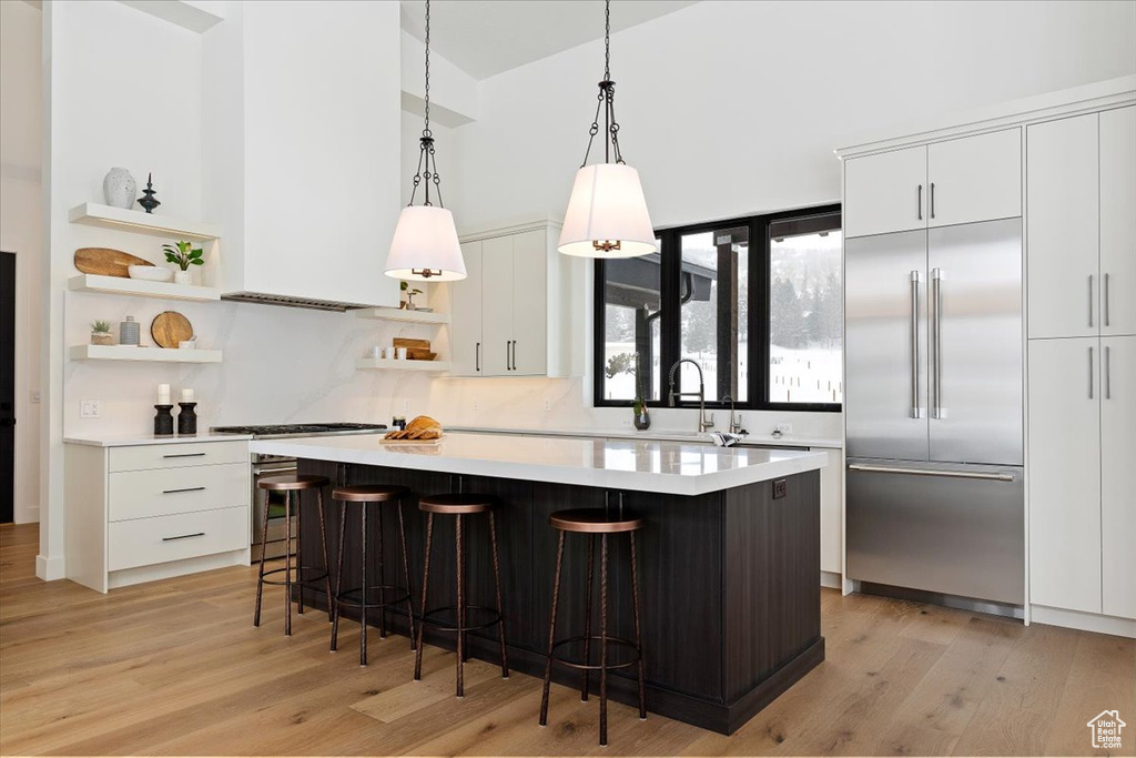 Kitchen with white cabinetry, stainless steel built in fridge, hanging light fixtures, and light wood-type flooring