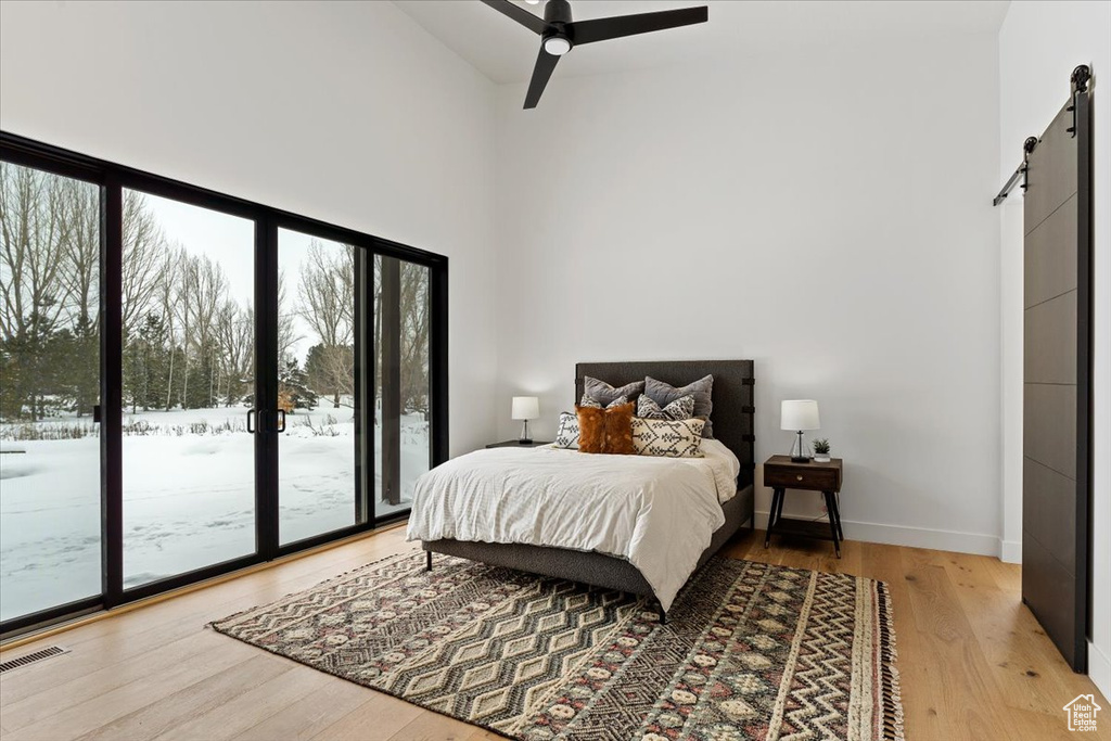 Bedroom featuring access to outside, a high ceiling, a barn door, light hardwood / wood-style flooring, and ceiling fan