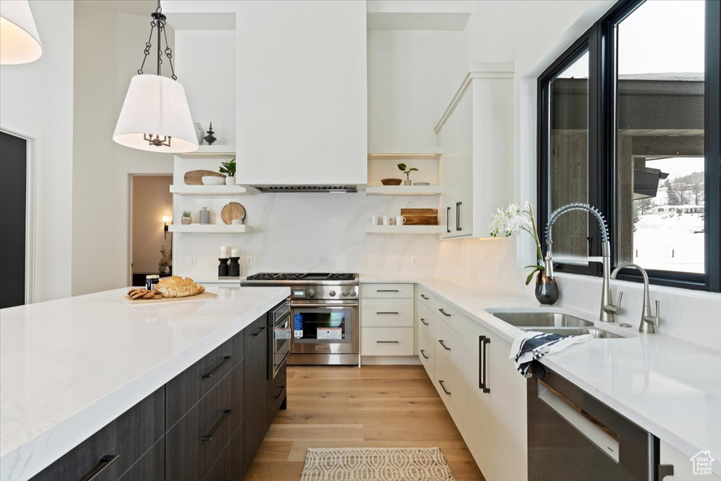 Kitchen featuring white cabinets, light hardwood / wood-style floors, decorative light fixtures, backsplash, and range with two ovens