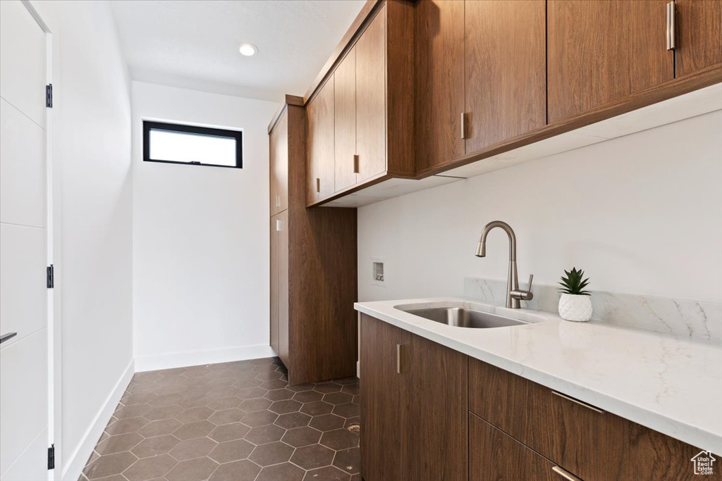 Laundry room featuring sink, cabinets, and dark tile floors