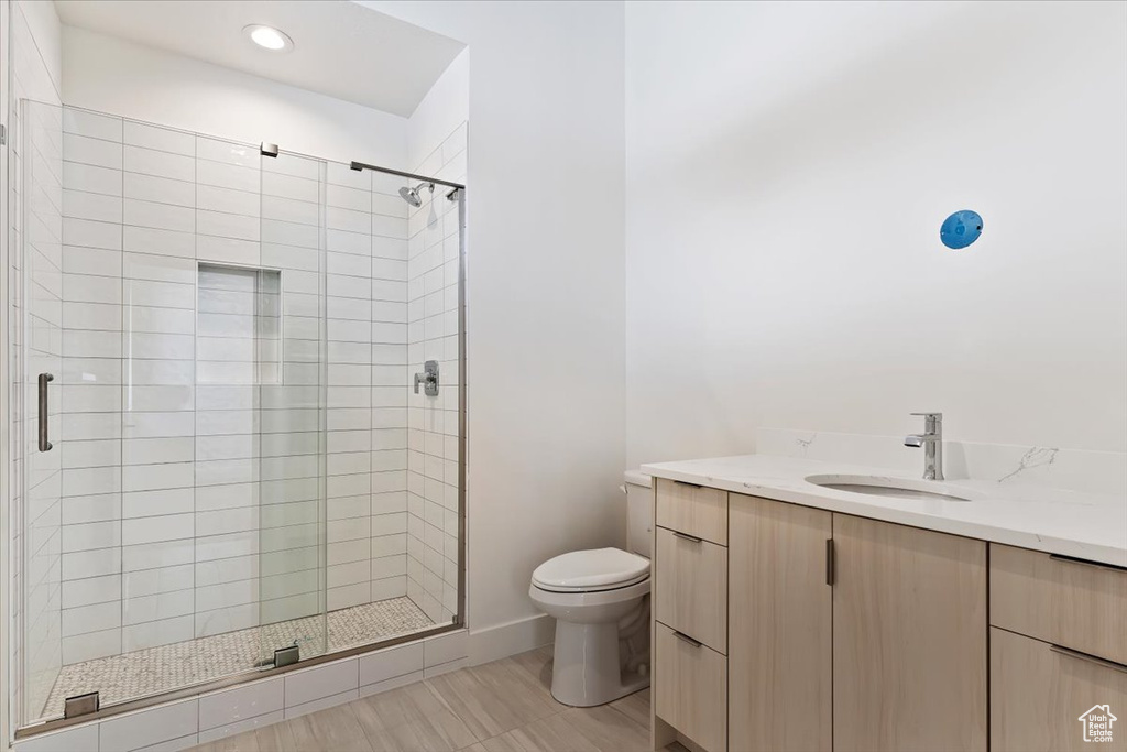 Bathroom featuring a shower with shower door, tile flooring, toilet, and vanity