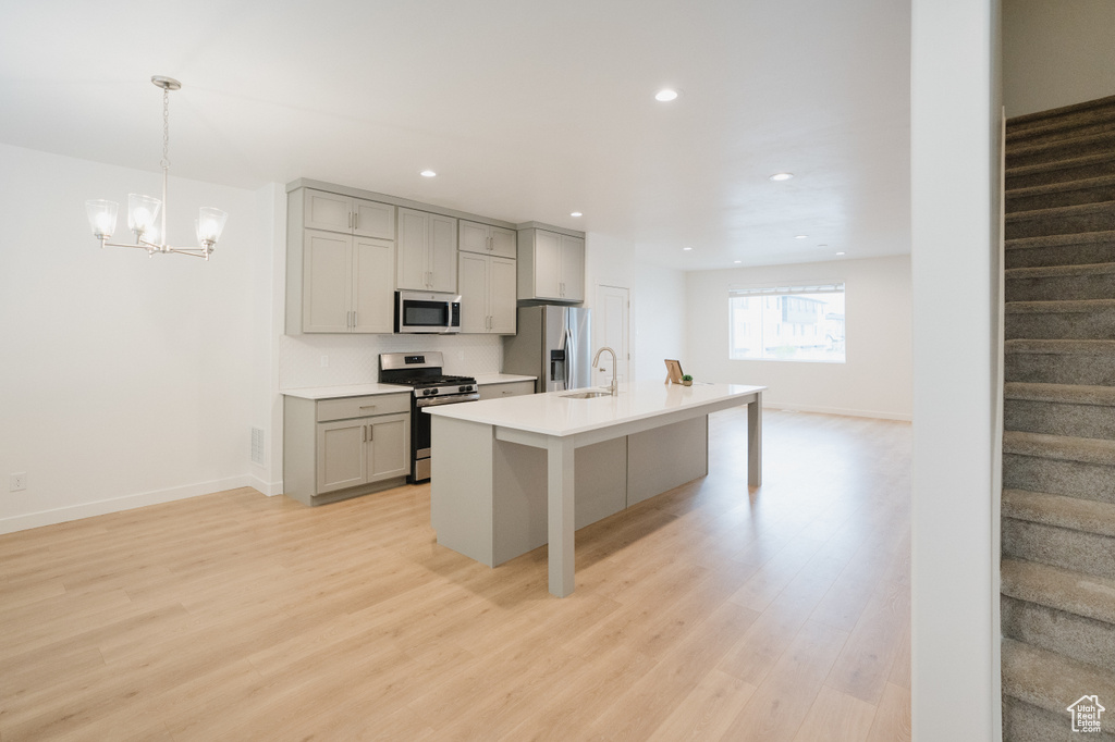 Kitchen featuring appliances with stainless steel finishes, light hardwood / wood-style flooring, gray cabinets, hanging light fixtures, and a breakfast bar