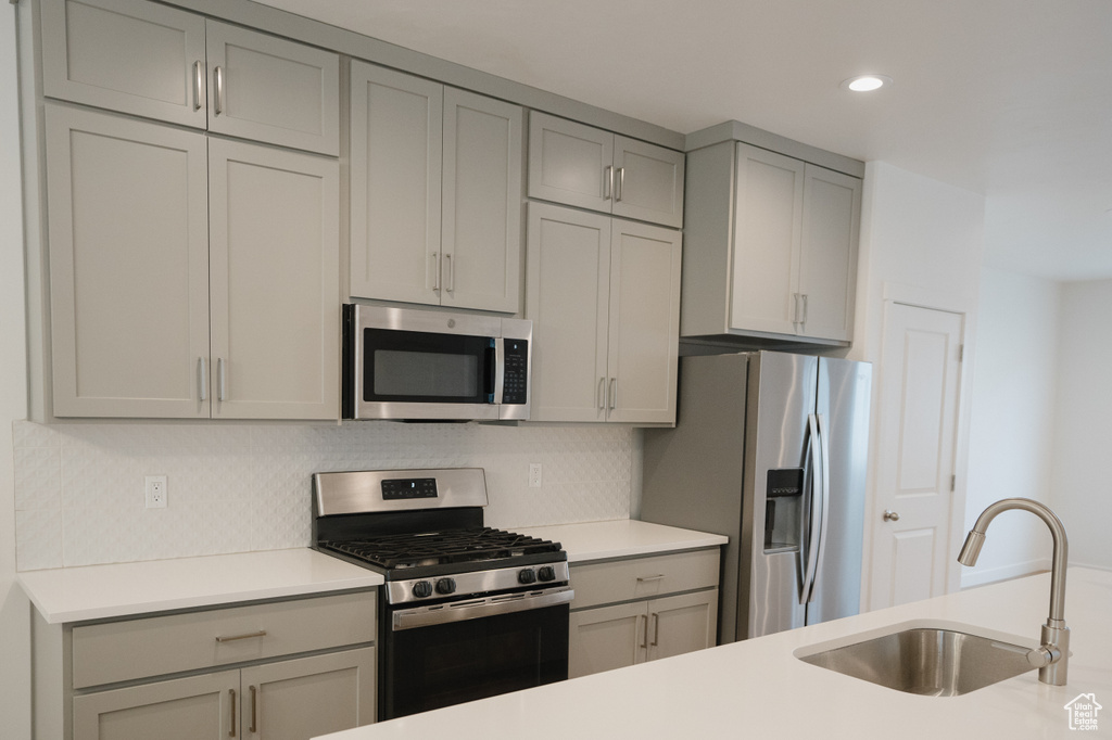 Kitchen featuring backsplash, sink, stainless steel appliances, and gray cabinetry