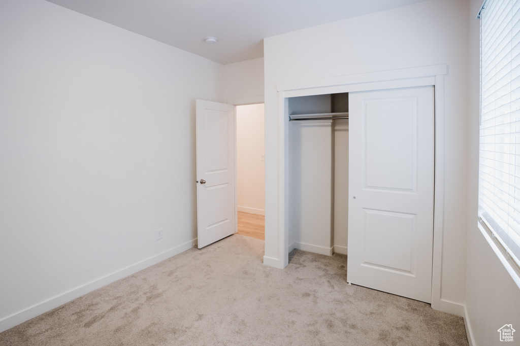 Unfurnished bedroom featuring light carpet, a closet, and multiple windows