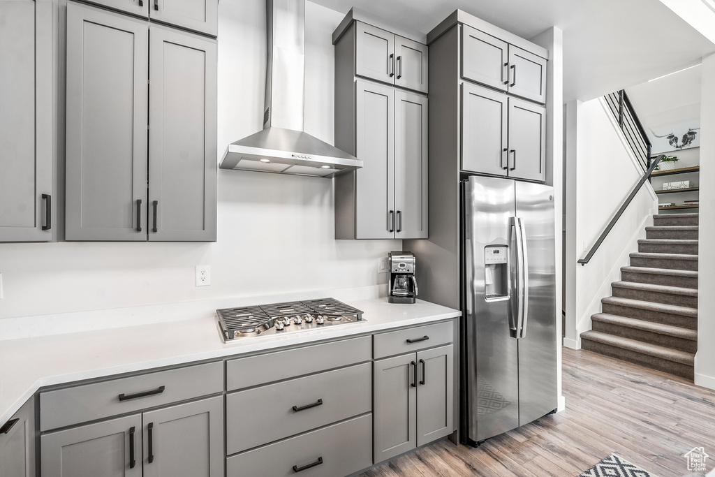 Kitchen featuring appliances with stainless steel finishes, light wood-type flooring, gray cabinetry, and wall chimney exhaust hood