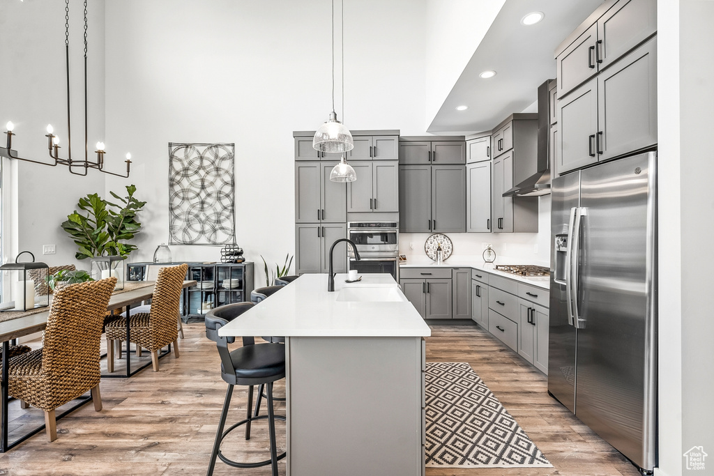Kitchen featuring an island with sink, appliances with stainless steel finishes, light hardwood / wood-style flooring, and hanging light fixtures
