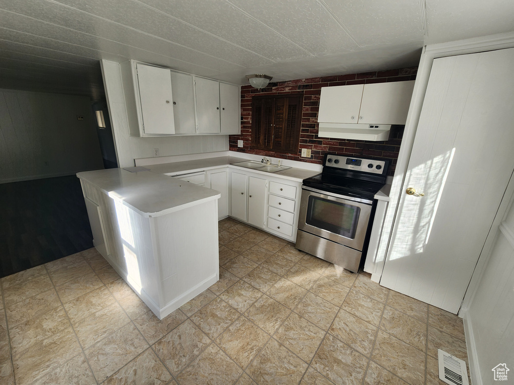Kitchen with light tile flooring, stainless steel electric range oven, brick wall, white cabinetry, and sink
